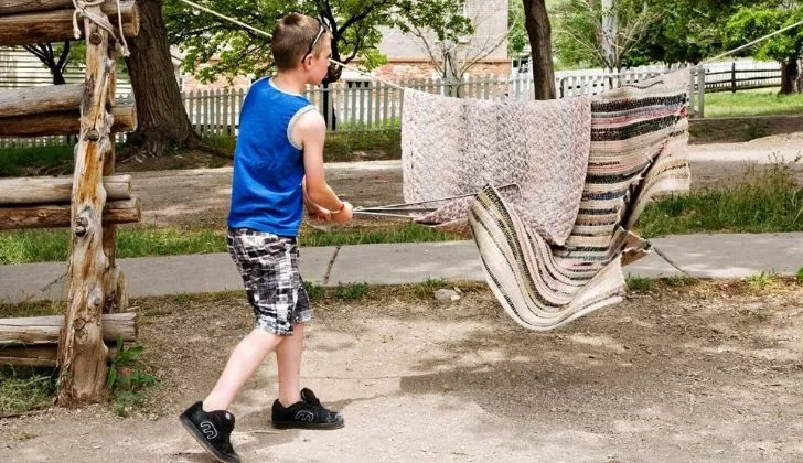 A boy hitting a rug on a washing line