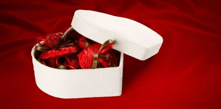 A white heart shapes box with chocolate inside individually wrapped in deep red paper
