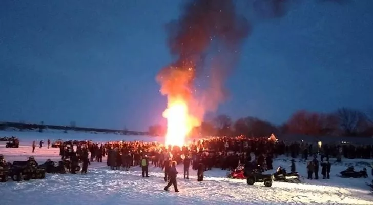 A snowman up in flames with lots of people watching