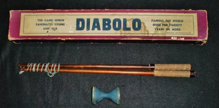 A vintage diabolo game set including an old box, sticks and spool.