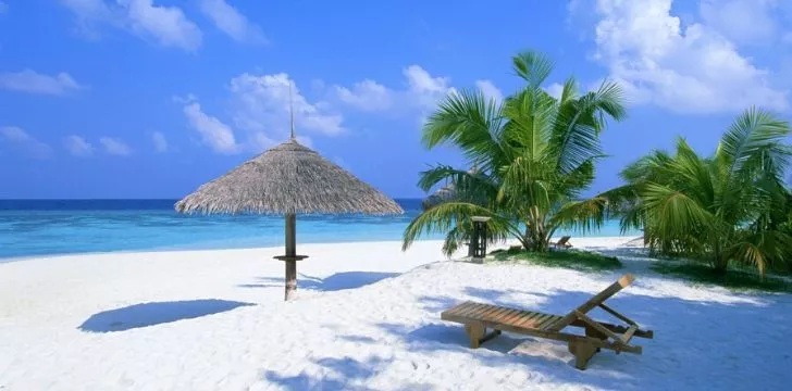 A sun lounger sitting on a white beach with a clear sunny blue sky