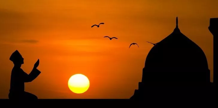 Prayer at dusk with a temple and birds flying in the sky.