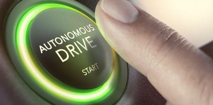 Someone about to press a green button in a car that reads "autonomous drive - start"