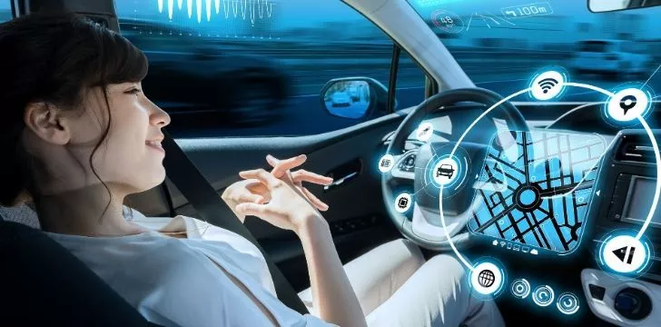 A woman sitting in her car with lots of pictures on the steering wheel showing a driverless cars possibilities