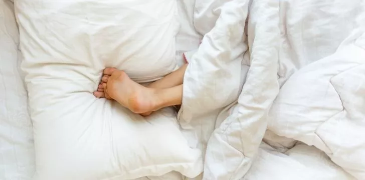 Someone upside down in bed with their feet on the pillows