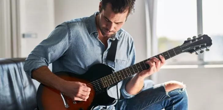 A man learning to play a guitar sitting on the sofa