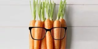 Carrots on a woodern background wearing glasses.