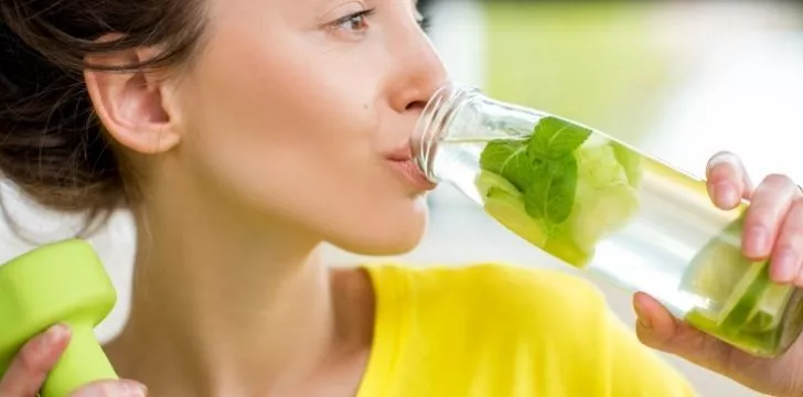A woman with nice skin drinking water from a glass bottle