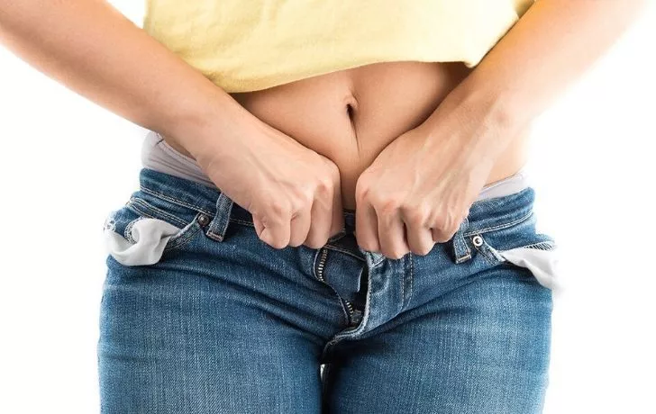 A woman struggling to zip and button her tight jeans