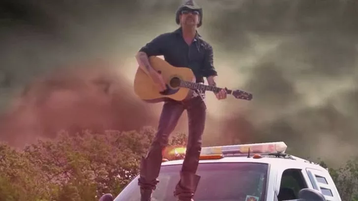 Joe Exotic standing on a police car with his guitar