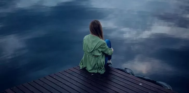 A depressed woman sitting on a dock looking over a lake