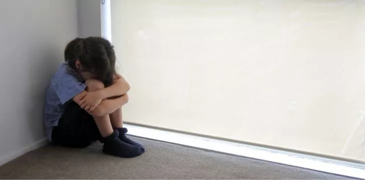 A young girl sat on the floor looking sad with her head in her lap