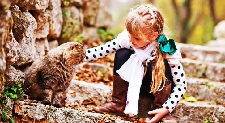 A child petting a cat outdoors