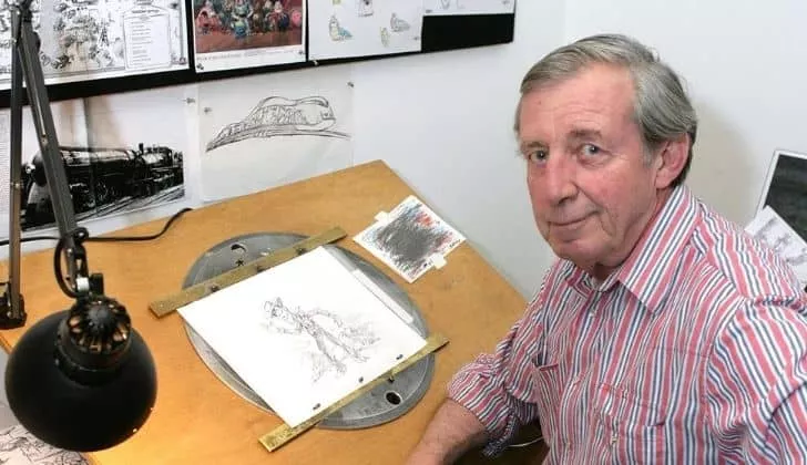 A photo of Bud Luckey who created Woody. On the table in front of him is an illustration of Woody