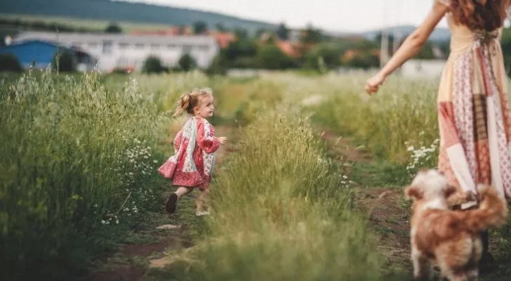 A toddler running across a grass field with her mother