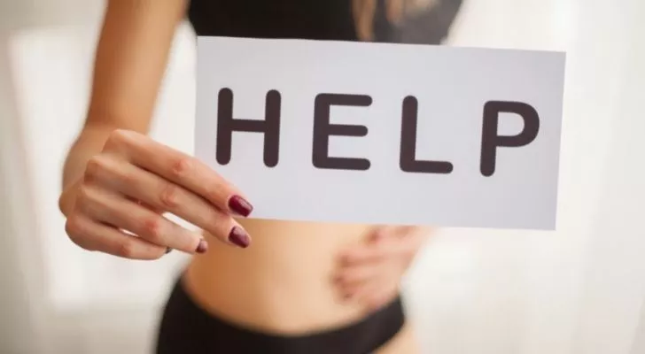 A woman holding her stomach with one hand and a "HELP" sign in the other