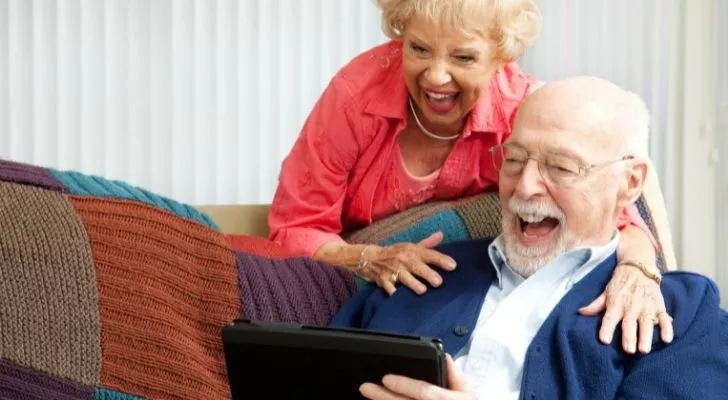 An older couple watching something on a pad and laughing