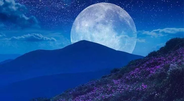 A full June moon behind mountains