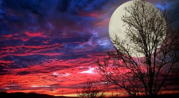 A full moon with a rich pink, red and purple sky