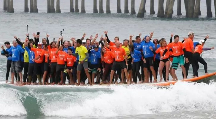 66 people on one big surfboard riding a wave