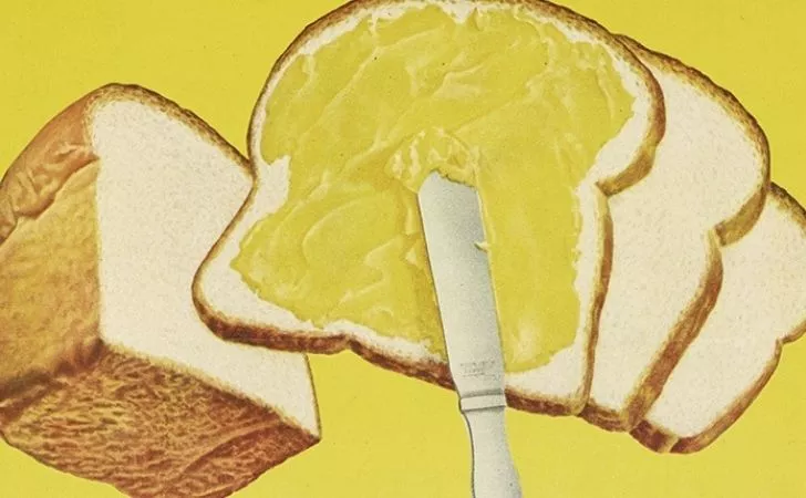 Yellow margarine being spread on sliced bread