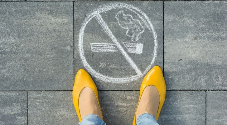 A woman standing over a no smoking sign on a pavement