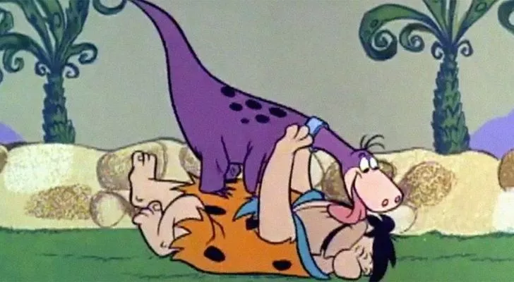 Fred Flintstone being licked by his pet dinosaur