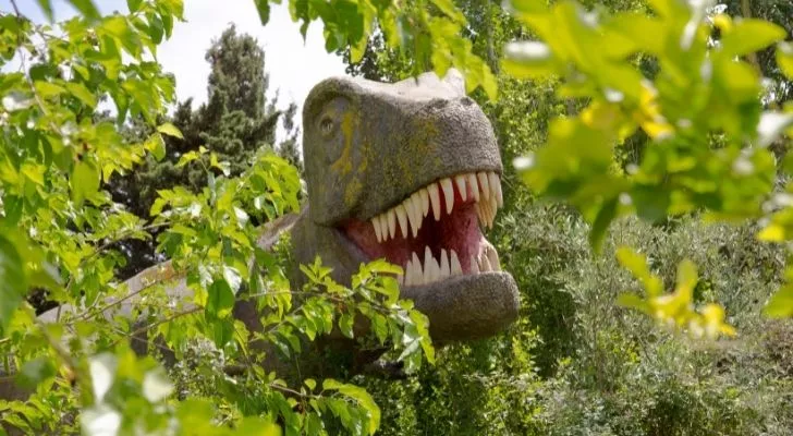 A T-rex head behind tree foliage
