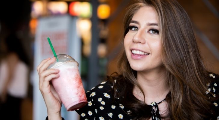 A woman smiling while she enjoys a strawberry frappé