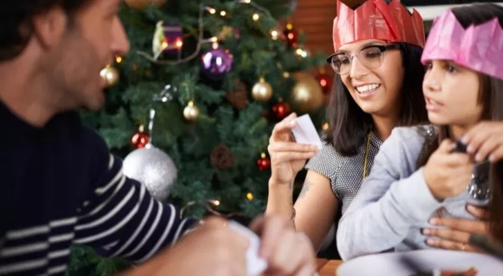 A family sharing a Christmas cracker joke together by the Christmas tree