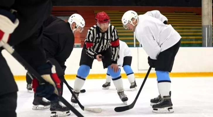 Hockey referee holding the puck between two players.