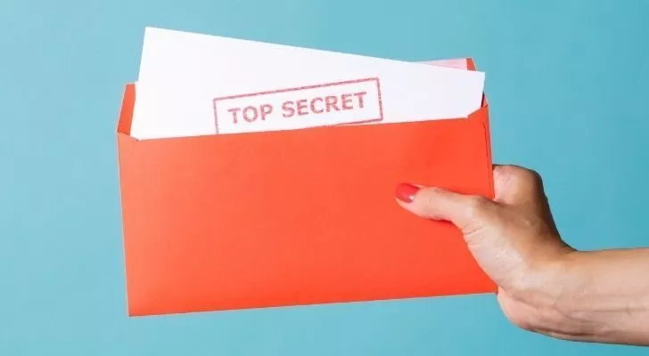 Person holding a piece of paper with the words "top secret" written on it.