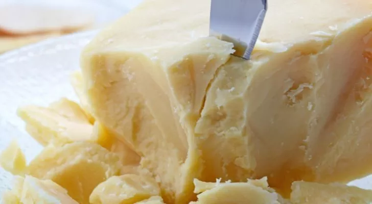 A knife slicing into a crumbly piece of parmesan