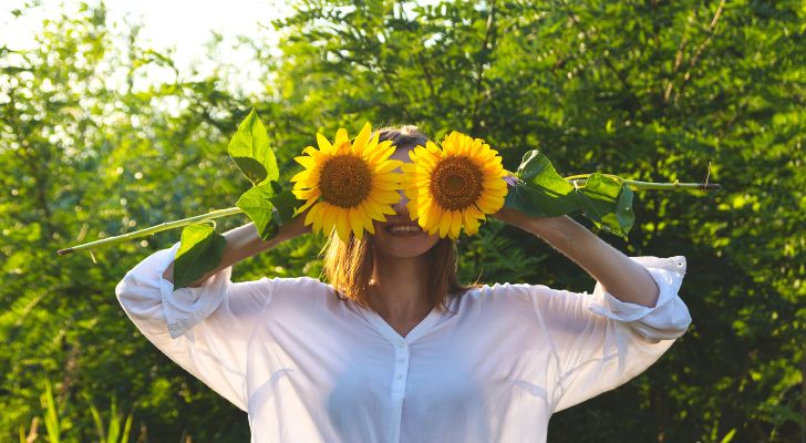 A person holding two sunflowers to their face.