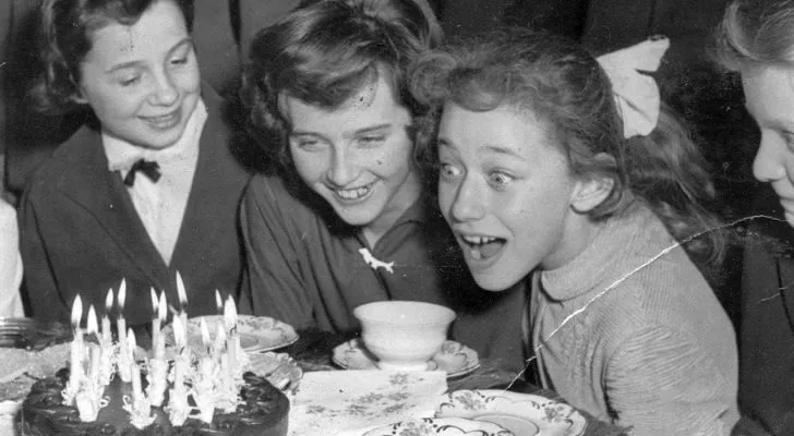 A black and white photo of a family celebrating a girls birthday with a cake