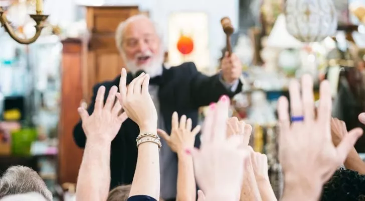 An auctioneer chanting to a crowd. Many people in the crowd are holding their hands up to bid.