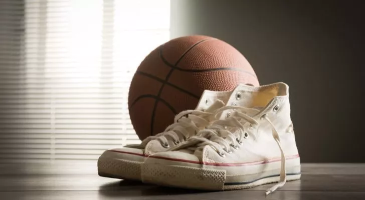 White low-cut Converse shoes lying next to a basketball