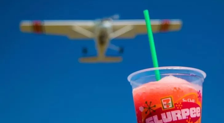 A red-colored slurpee in the foreground, with a blurred planed flying in the background