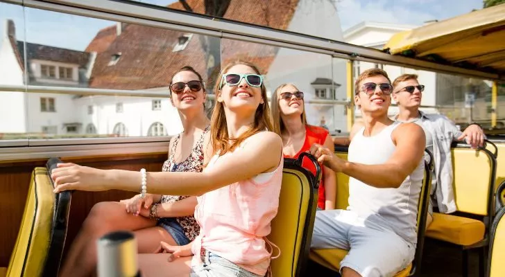 A group of tourists on the top deck of a bus enjoying the view and not wearing seatbelts