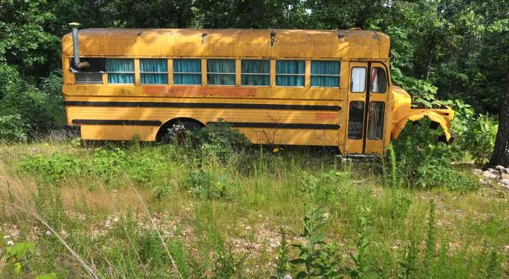 An old yellow school bus with curtains and a chimney in a field