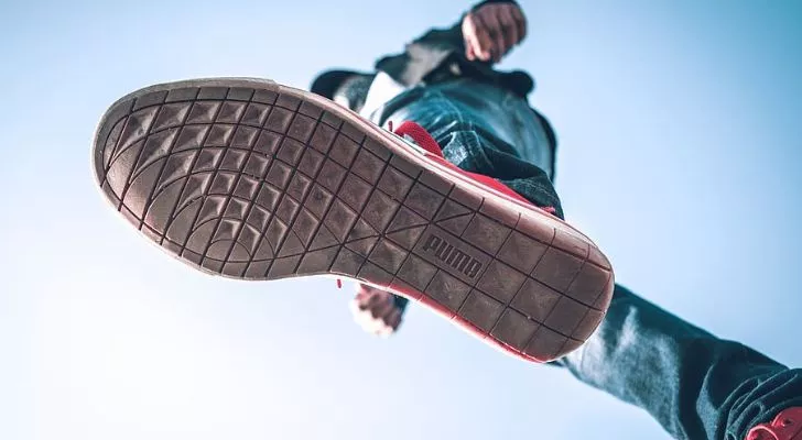 A man walking in Puma shoes, as seen from below. The Puma shoes have the brand's logo on the sole.