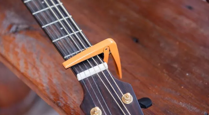 The head of a guitar with a capo pinching the strings on the neck