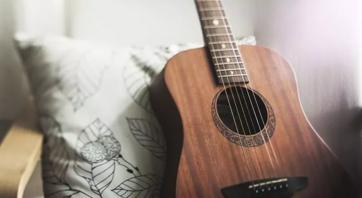 A brown guitar leans against a apillow