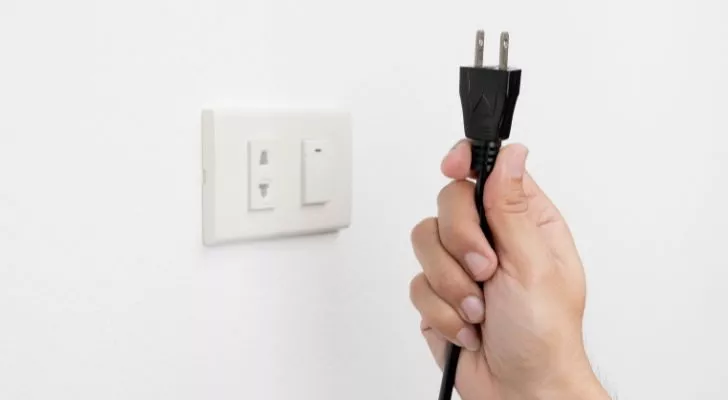 A hand holding a plug next to an electricity outlet