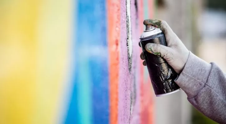 A hand holding a spray can and adding graffiti to a wall