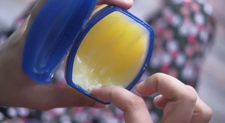 A person's finger scooping some vaseline out of a tub