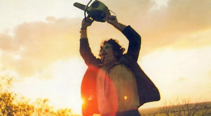 A wild looking man holds a chainsaw above his head