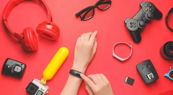 Various electronics and gadgets are laid on a table as a person tries on a smart watch