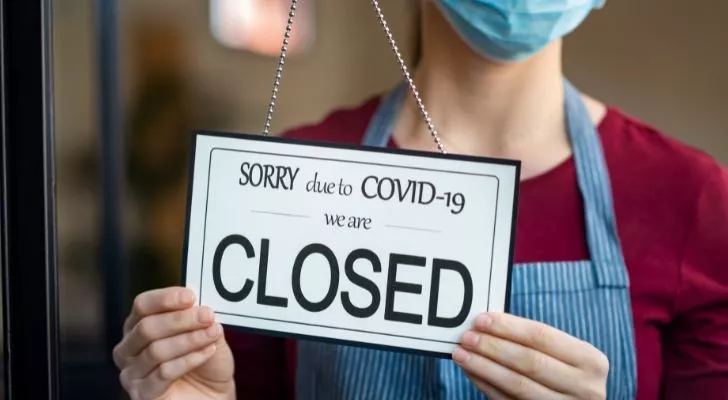 A woman in a mask puts a "closed due to COVID-19" sign in the window