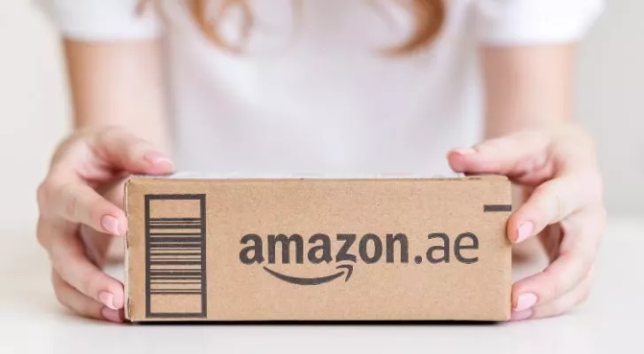 A woman holds a box which has "amazon.ae" printed on the side